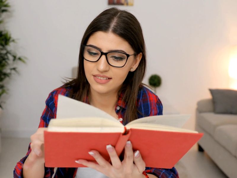 devojka sa naočarama sedi i čita knjigu