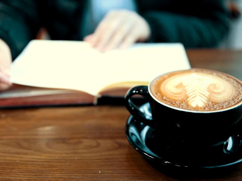 osoba čita knjigu i pije kafu